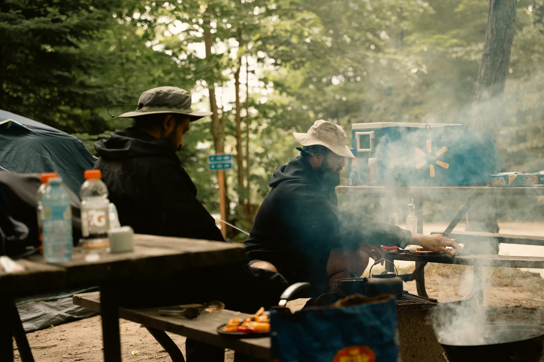 Outdoor camping scene with men cooking at a campsite with tents and trees.