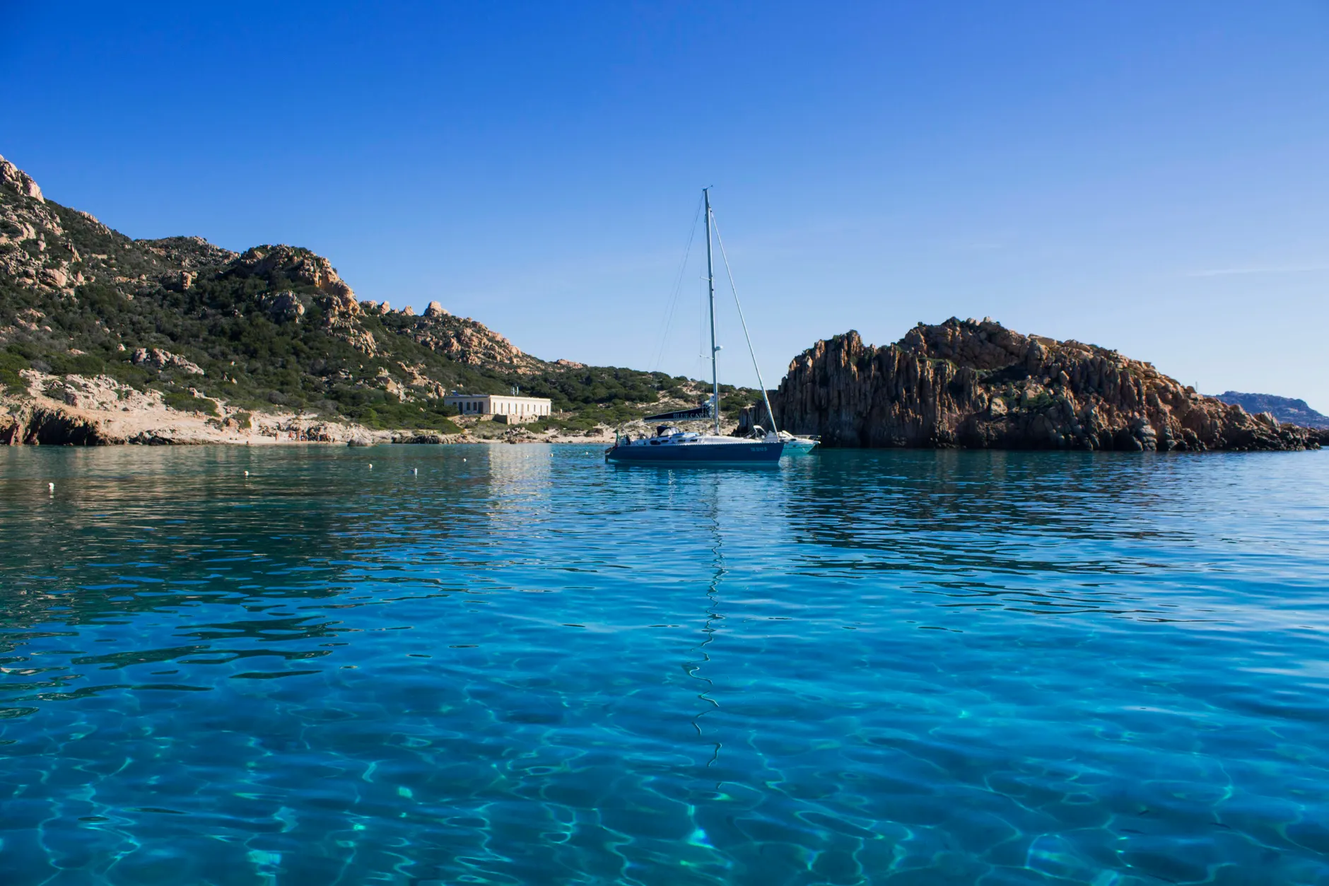 A sailboat floats tranquil in the clear blue waters of La Maddalena, Italy.
